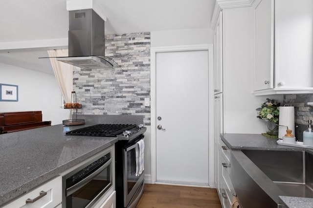 kitchen featuring hardwood / wood-style floors, backsplash, white cabinetry, stainless steel appliances, and island range hood