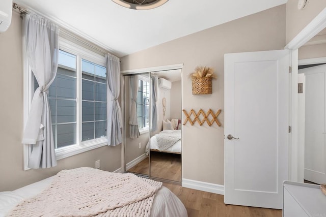 bedroom with light wood-type flooring, a closet, and a wall mounted AC