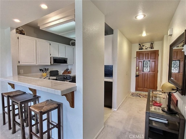 kitchen with tile countertops, gas range, a breakfast bar area, white cabinetry, and recessed lighting