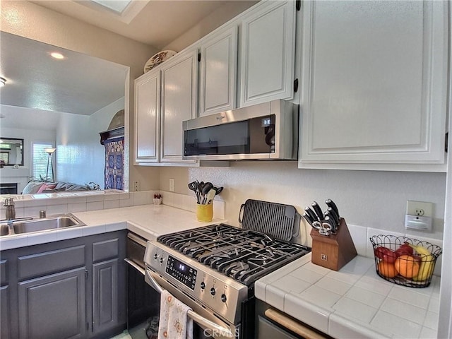 kitchen with tile countertops, a sink, white cabinetry, appliances with stainless steel finishes, and gray cabinets