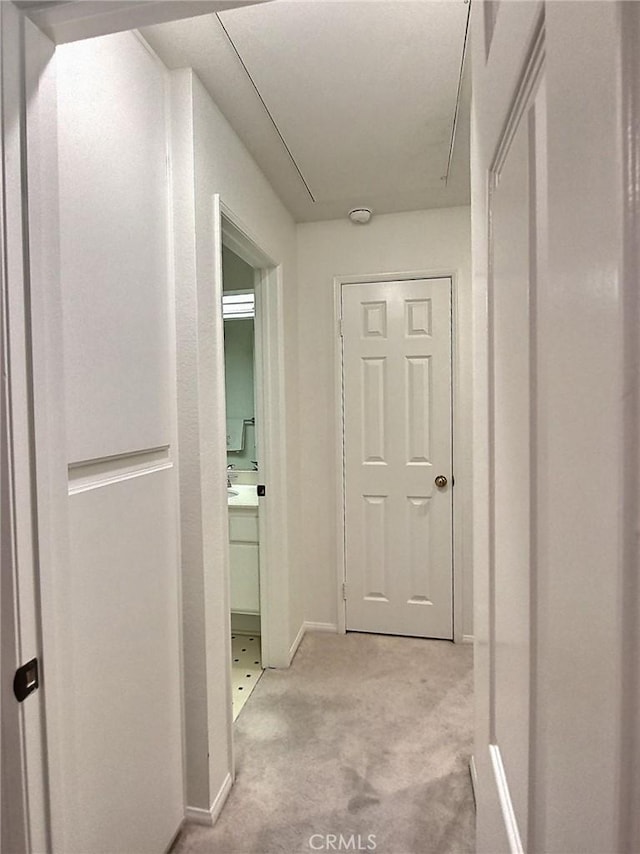 corridor featuring light carpet, attic access, and baseboards