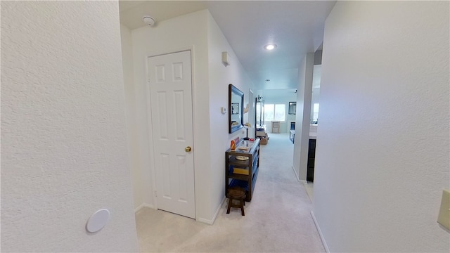 hallway featuring light colored carpet, a textured wall, and baseboards