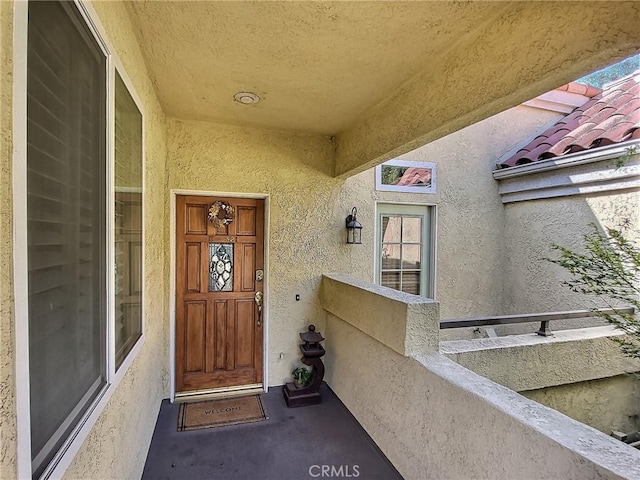 entrance to property with a tile roof, a balcony, and stucco siding