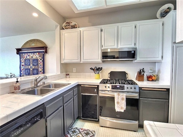 kitchen featuring tile countertops, gray cabinets, stainless steel appliances, a sink, and recessed lighting