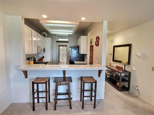 kitchen featuring freestanding refrigerator, white cabinetry, tile countertops, and a kitchen breakfast bar