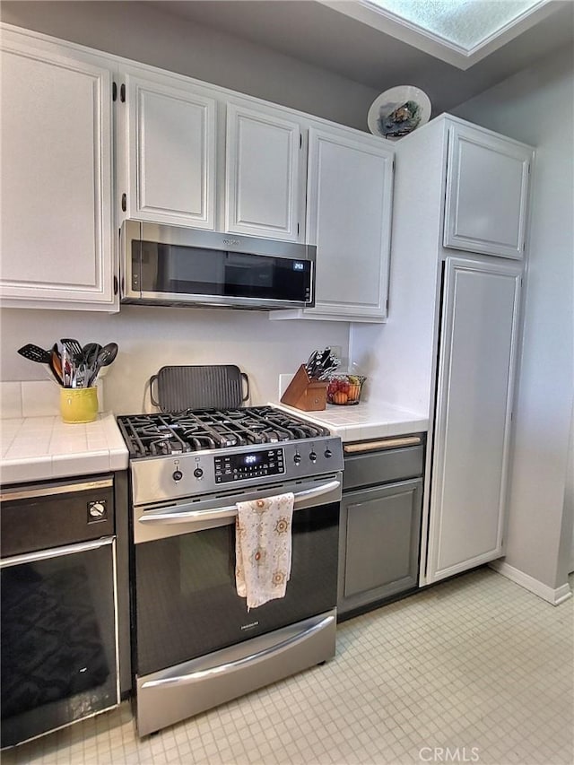 kitchen with tile countertops, stainless steel appliances, and white cabinetry