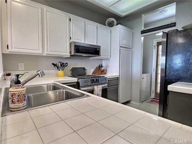 kitchen featuring a sink, white cabinets, appliances with stainless steel finishes, tile counters, and washer / dryer