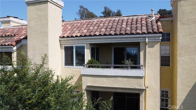 rear view of property with a tiled roof, a chimney, a balcony, and stucco siding