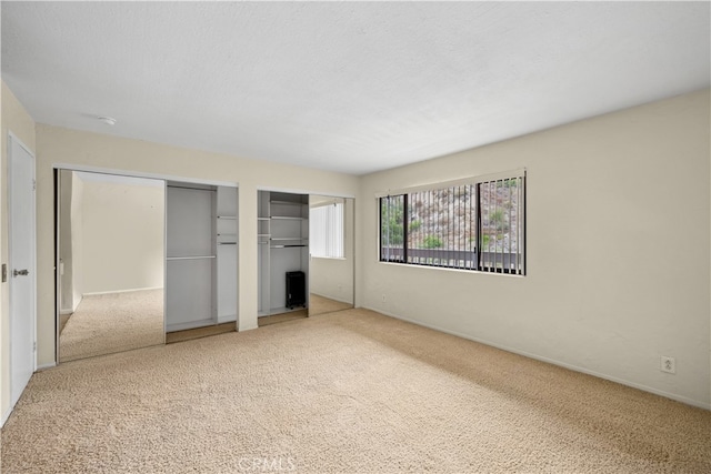 unfurnished bedroom with multiple closets and light colored carpet