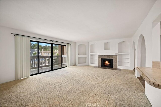 unfurnished living room featuring a tile fireplace, built in features, and carpet