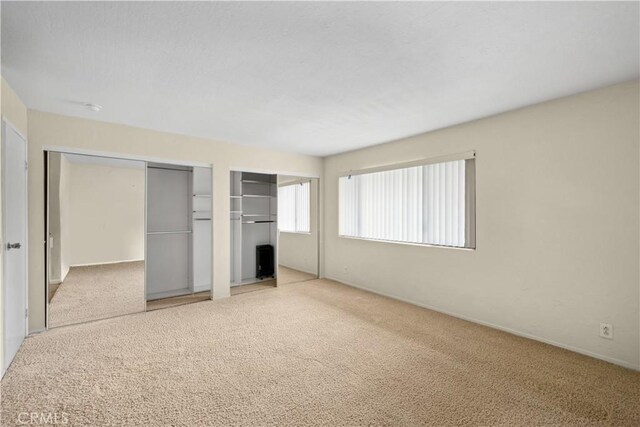 unfurnished bedroom featuring multiple closets and light colored carpet