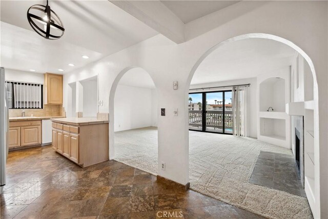 kitchen with decorative backsplash, light brown cabinetry, dishwasher, beamed ceiling, and dark tile patterned flooring