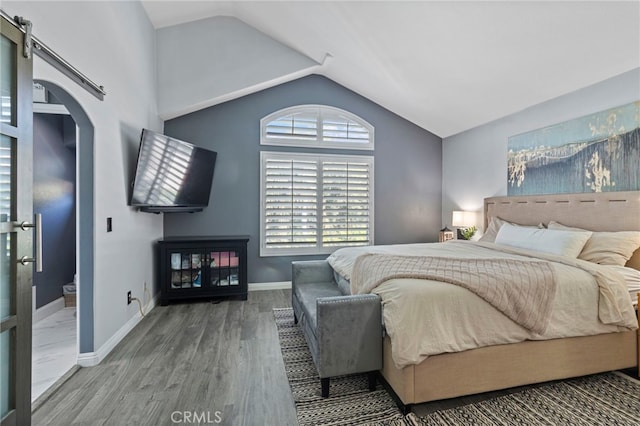 bedroom featuring ensuite bath, hardwood / wood-style floors, a barn door, and high vaulted ceiling