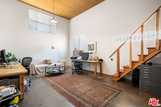 home office featuring concrete flooring and a towering ceiling