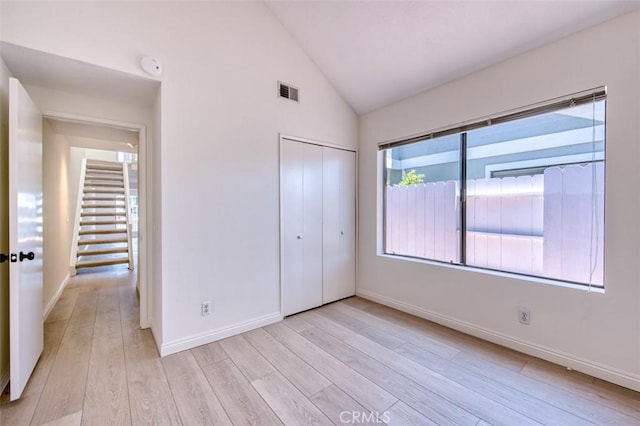 unfurnished bedroom with light hardwood / wood-style floors, high vaulted ceiling, and a closet