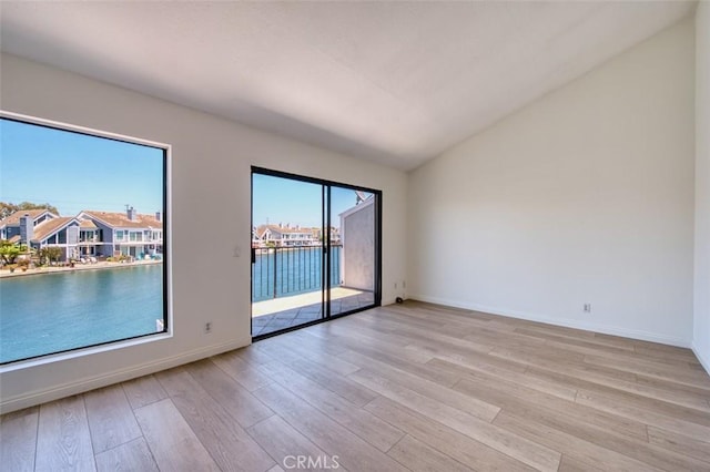 spare room featuring a water view, light wood-type flooring, and vaulted ceiling