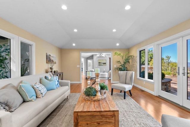 living room featuring vaulted ceiling, a notable chandelier, light wood-type flooring, and french doors