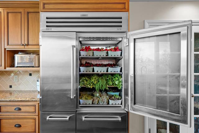 interior space featuring high end refrigerator, light stone countertops, and backsplash