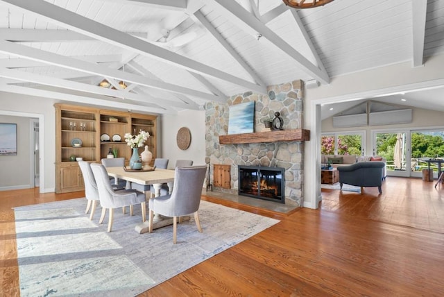 dining space featuring vaulted ceiling with beams, a stone fireplace, and hardwood / wood-style flooring