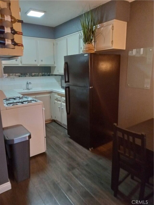 kitchen featuring dark hardwood / wood-style flooring, black fridge, and white cabinets