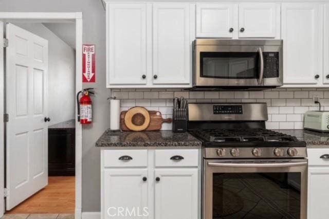 kitchen featuring white cabinetry, appliances with stainless steel finishes, and dark stone counters