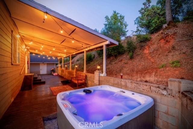 patio terrace at dusk featuring a wooden deck and a hot tub