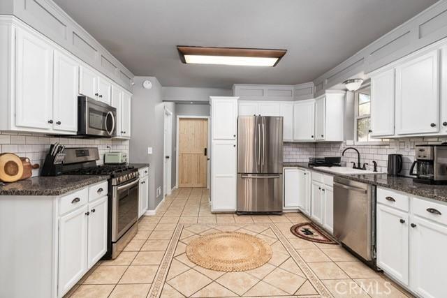 kitchen with light tile patterned floors, stainless steel appliances, sink, and white cabinets