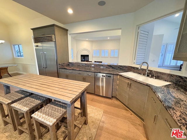 kitchen with sink, light hardwood / wood-style flooring, gray cabinets, dark stone countertops, and appliances with stainless steel finishes