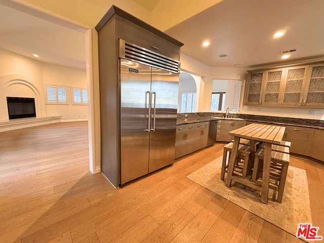 kitchen with a fireplace, light wood-type flooring, stainless steel appliances, and sink