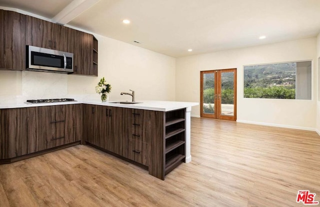 kitchen with dark brown cabinetry, sink, stainless steel appliances, kitchen peninsula, and light hardwood / wood-style floors