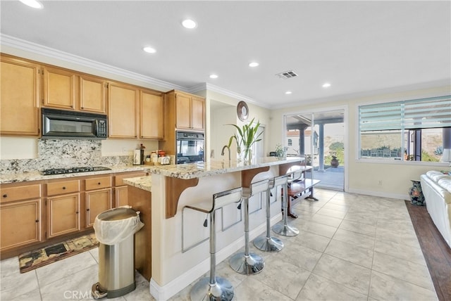 kitchen with backsplash, a kitchen island with sink, black appliances, crown molding, and light stone countertops