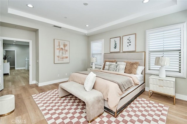 bedroom with visible vents, baseboards, a tray ceiling, light wood-style floors, and recessed lighting