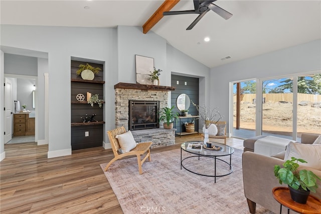 living room featuring ceiling fan, light hardwood / wood-style flooring, a stone fireplace, high vaulted ceiling, and beam ceiling