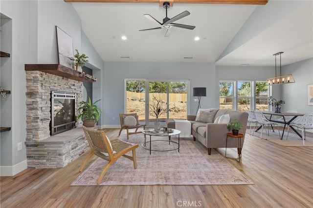 living room featuring ceiling fan, beam ceiling, light wood-type flooring, and a stone fireplace