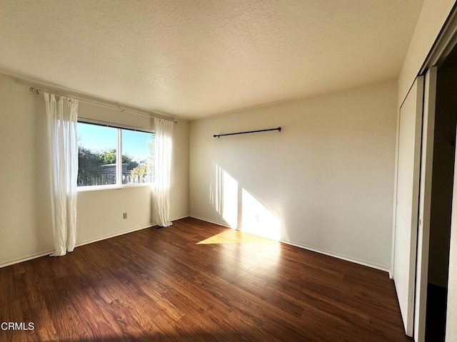 unfurnished room featuring dark wood-type flooring and a textured ceiling