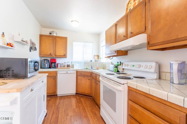 kitchen with tile counters, sink, light wood-type flooring, and white appliances