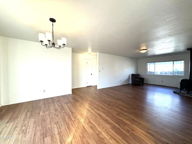 unfurnished living room with a wood stove, a textured ceiling, a notable chandelier, and dark wood-type flooring