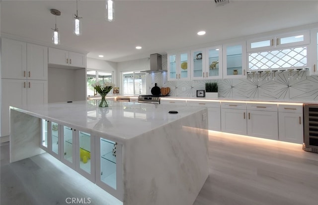 kitchen featuring white cabinetry, tasteful backsplash, wall chimney exhaust hood, pendant lighting, and a spacious island