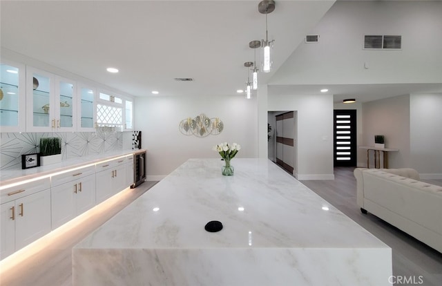 kitchen with pendant lighting, white cabinets, light stone counters, and light wood-type flooring