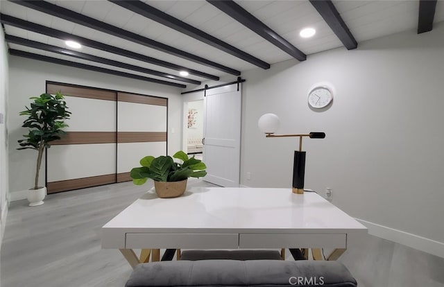 home office with light hardwood / wood-style floors, beamed ceiling, and a barn door