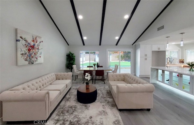 living room featuring beamed ceiling, light hardwood / wood-style flooring, sink, and high vaulted ceiling