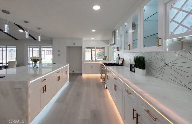 kitchen with stainless steel range, light wood-type flooring, backsplash, and white cabinetry