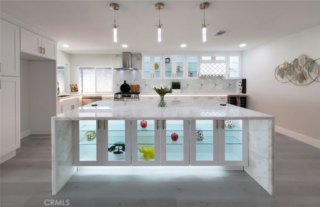 kitchen featuring decorative backsplash, white cabinets, a center island, sink, and wall chimney range hood