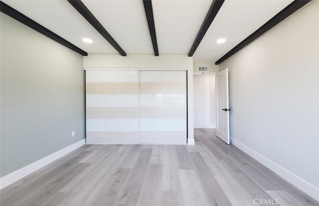 unfurnished bedroom with light hardwood / wood-style floors, beamed ceiling, and a closet