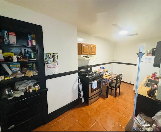 kitchen with light brown cabinetry, gas range, light tile patterned floors, and sink