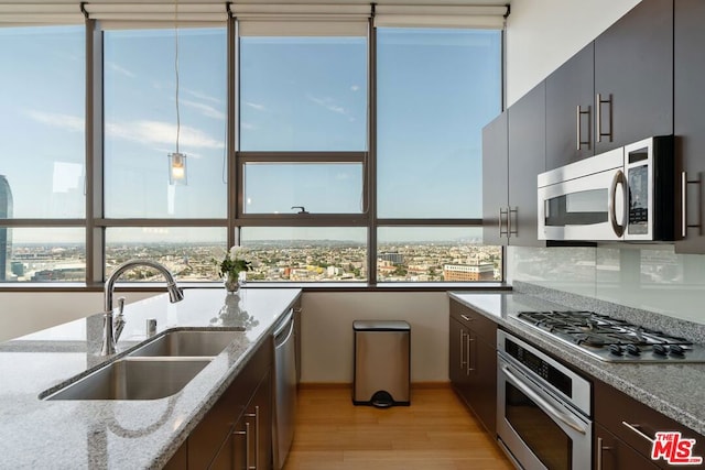 kitchen featuring appliances with stainless steel finishes, light hardwood / wood-style flooring, dark brown cabinets, sink, and light stone countertops