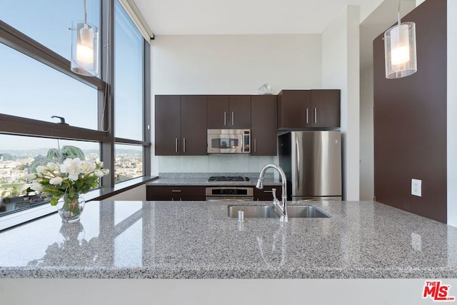 kitchen featuring stainless steel appliances, dark brown cabinetry, sink, light stone countertops, and pendant lighting