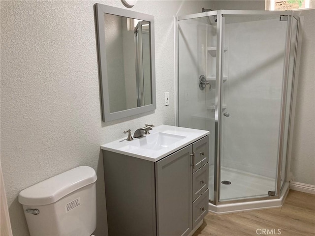 bathroom with hardwood / wood-style floors, vanity, a shower with shower door, and toilet