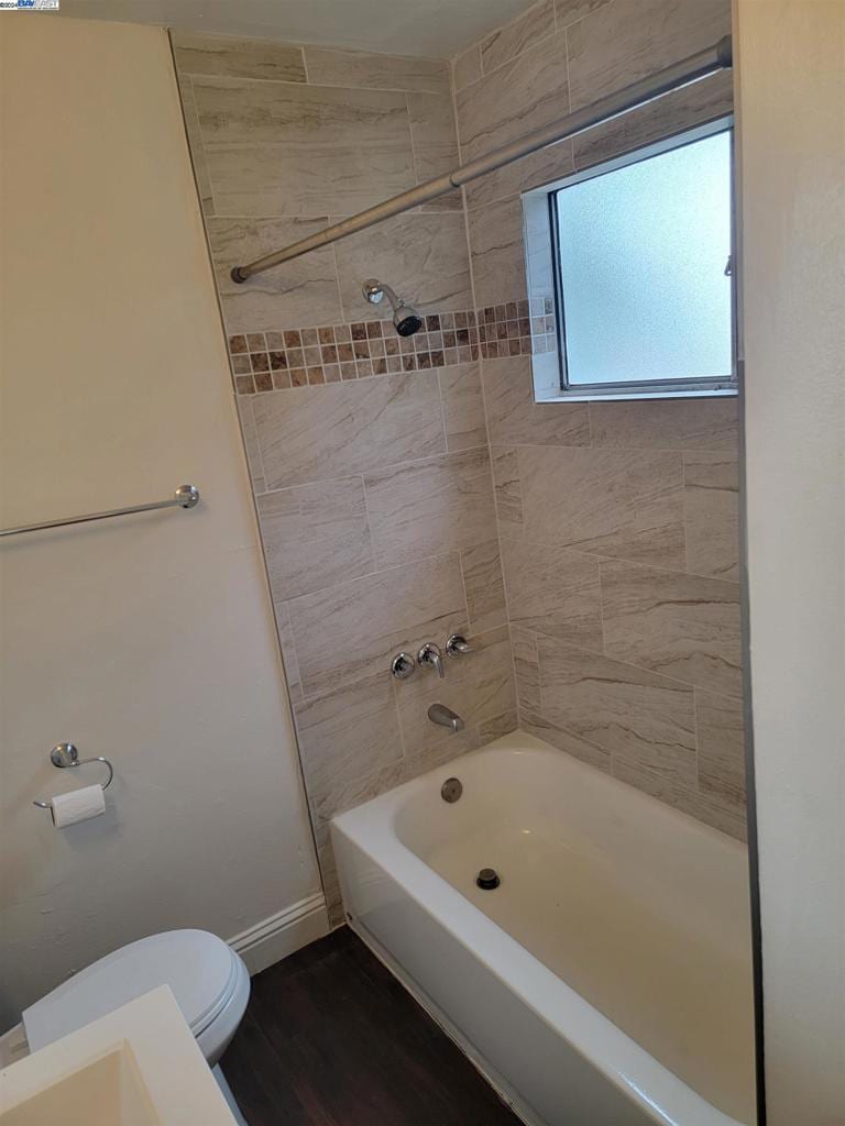 bathroom featuring tiled shower / bath combo, hardwood / wood-style flooring, and toilet