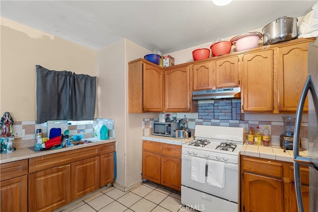 kitchen with light tile patterned flooring, tile counters, tasteful backsplash, and stainless steel appliances